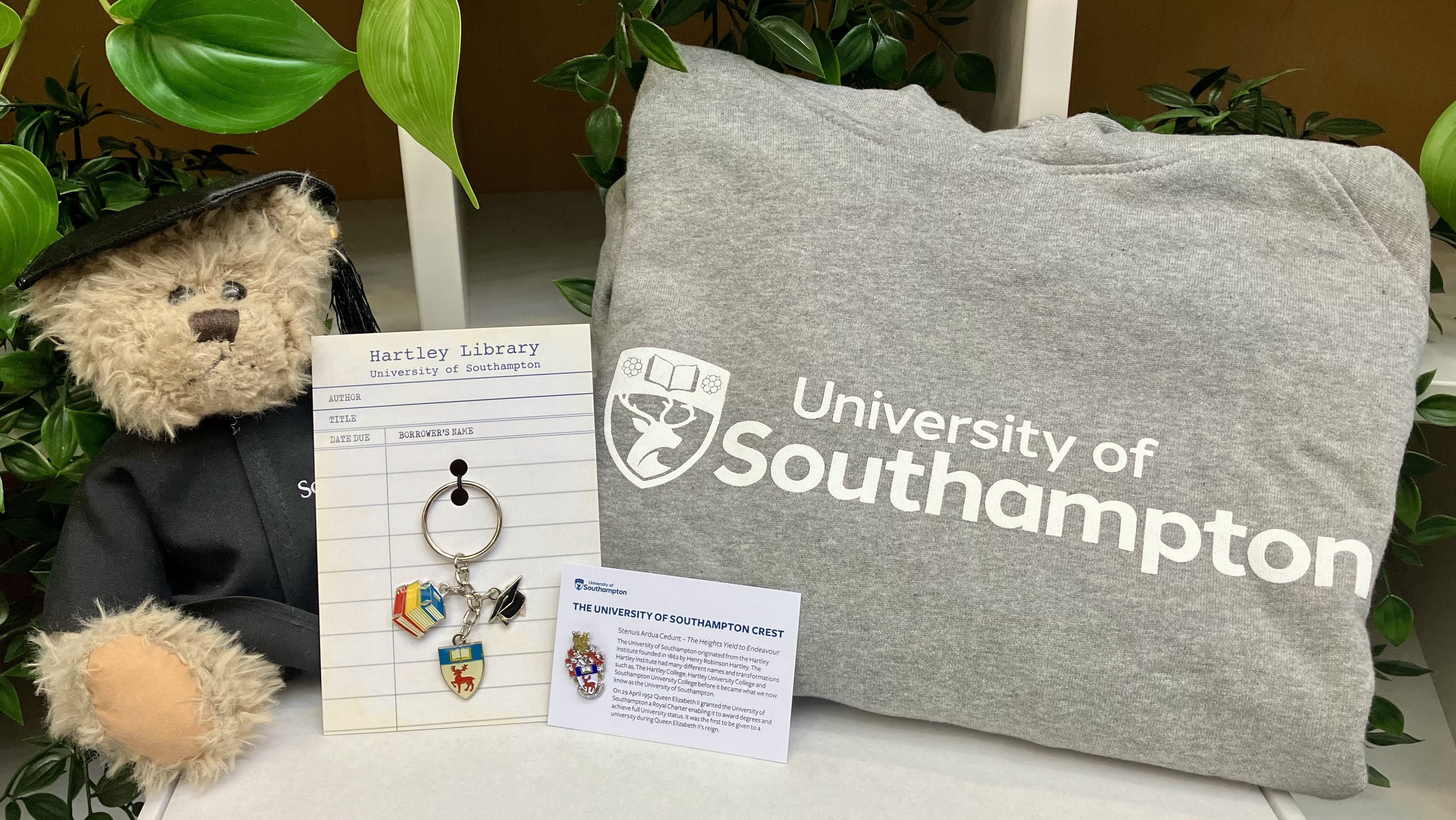 Hartley bear sitting on a table with the university keyring, pin and grey hoodie.
