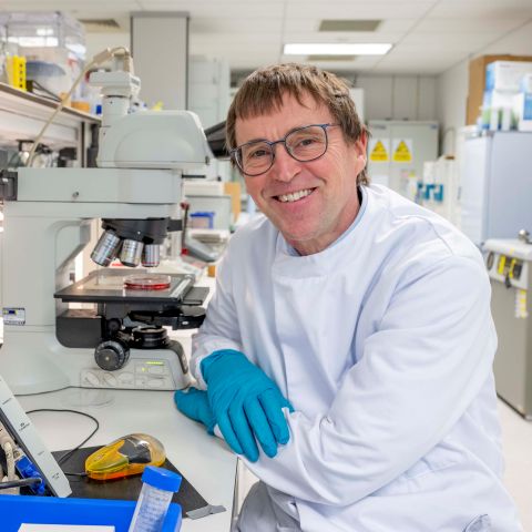 Professor Hywel Morgan smiling while working at a microscope in an IfLS lab.