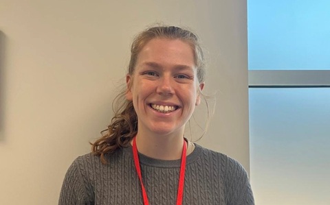 Head and shoulders photo of a woman with long hair in a pony tail, wearing a grey jumper and red lanyard