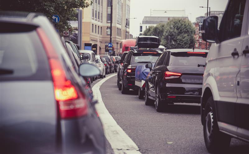 Cars seen from the rear, some with brake lights on, in heavy queuing traffic in a city street.