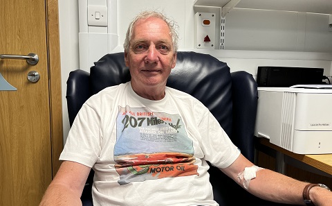 A man, Ian Robinson, sitting in a chair in a hospital consulting room with a dressing on his arm where blood has been taken