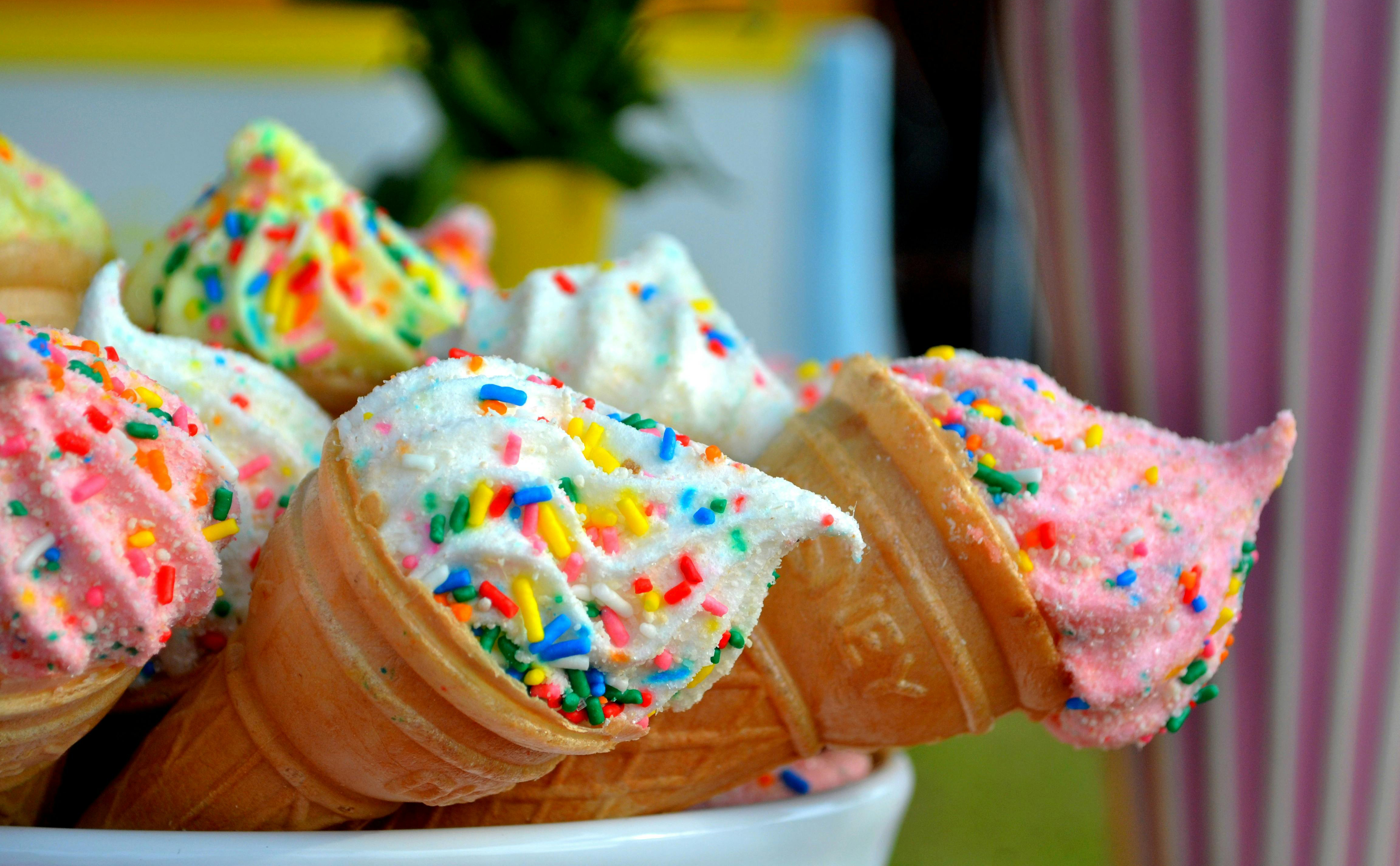 Three ice-cream cones arranged half lying down on a plate with multi-coloured ice-cream and sprinkles on top.