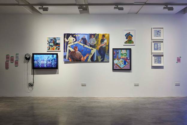 A gallery wall with several colourful artworks displayed, as well as a TV monitor showing artwork.
