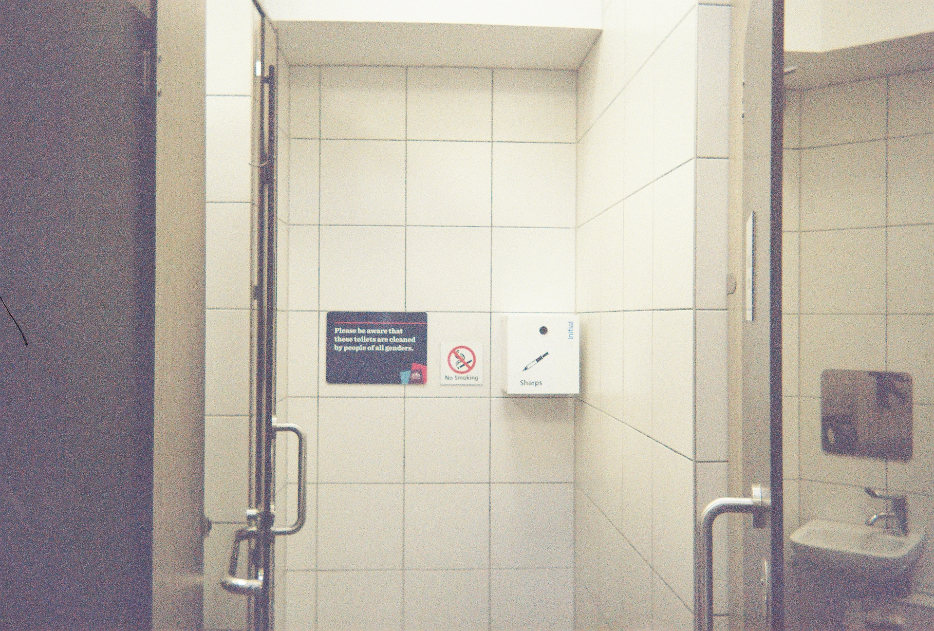 A tiled toilet wall with a sharps box attached.