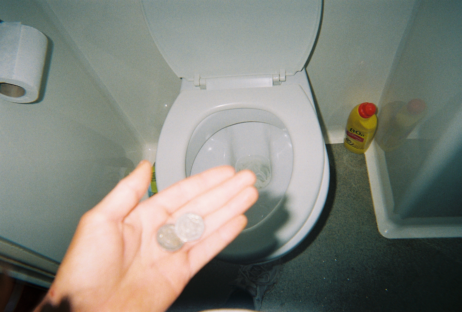 Hand holding coins in the foreground with a toilet bowl in the background