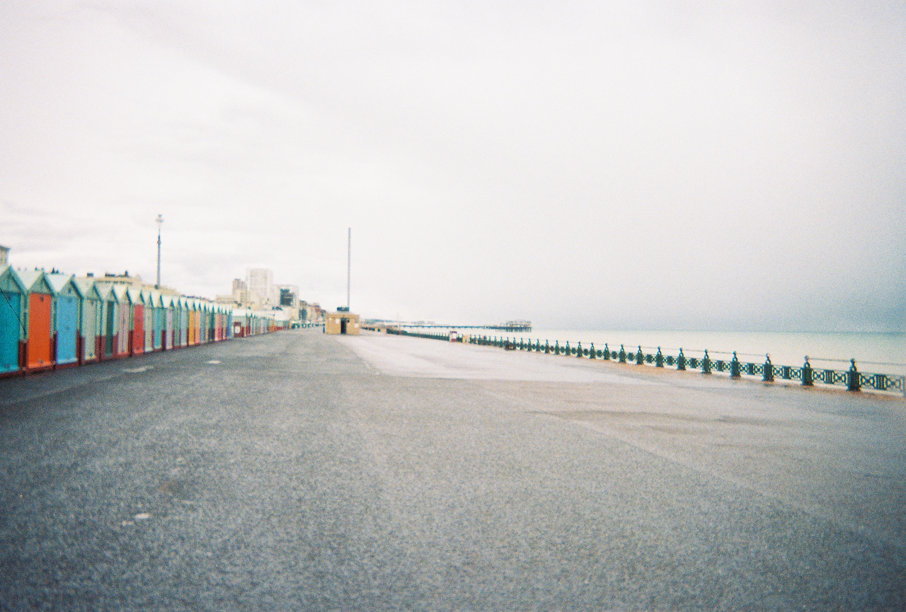 A long seafront path with multi-coloured beach huts on the left side.