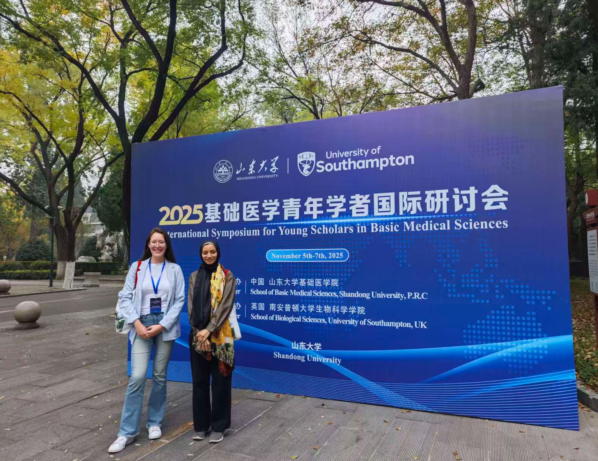 Polina and Yomna stood in front of a large digital sign advertising the symposium 