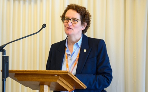 Woman with short dark hair and glasses standing at a lecturn speaking