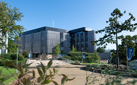 A wide open paved space in front of a large wood clad university building.