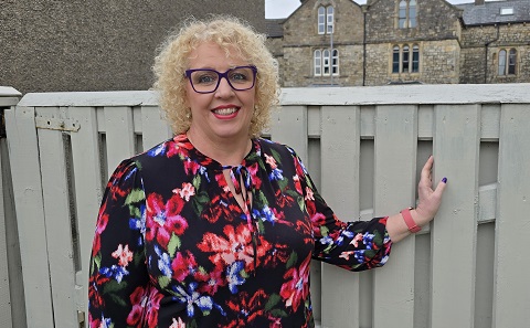 A woman (Karen) in a colourful top, standing by a garden fence