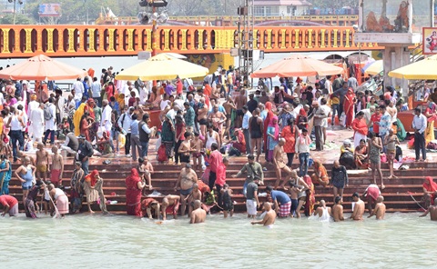 Dozens of people gathered at the edge of a large body of water. Some of the people are bathing in the water.