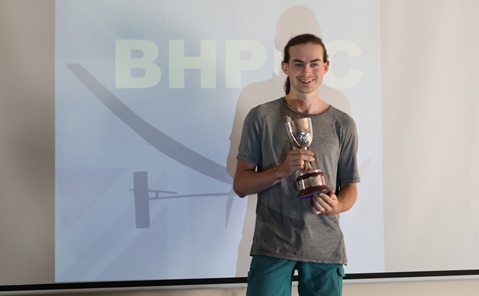 A man standing in front of a white projector screen, holding a cup
