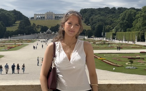 Young woman in a white sleeveless top standing outside in front of a large pedestrianised and green area