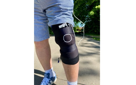 Close up of a man’s knee, wearing a black elastic support with wires coming off it