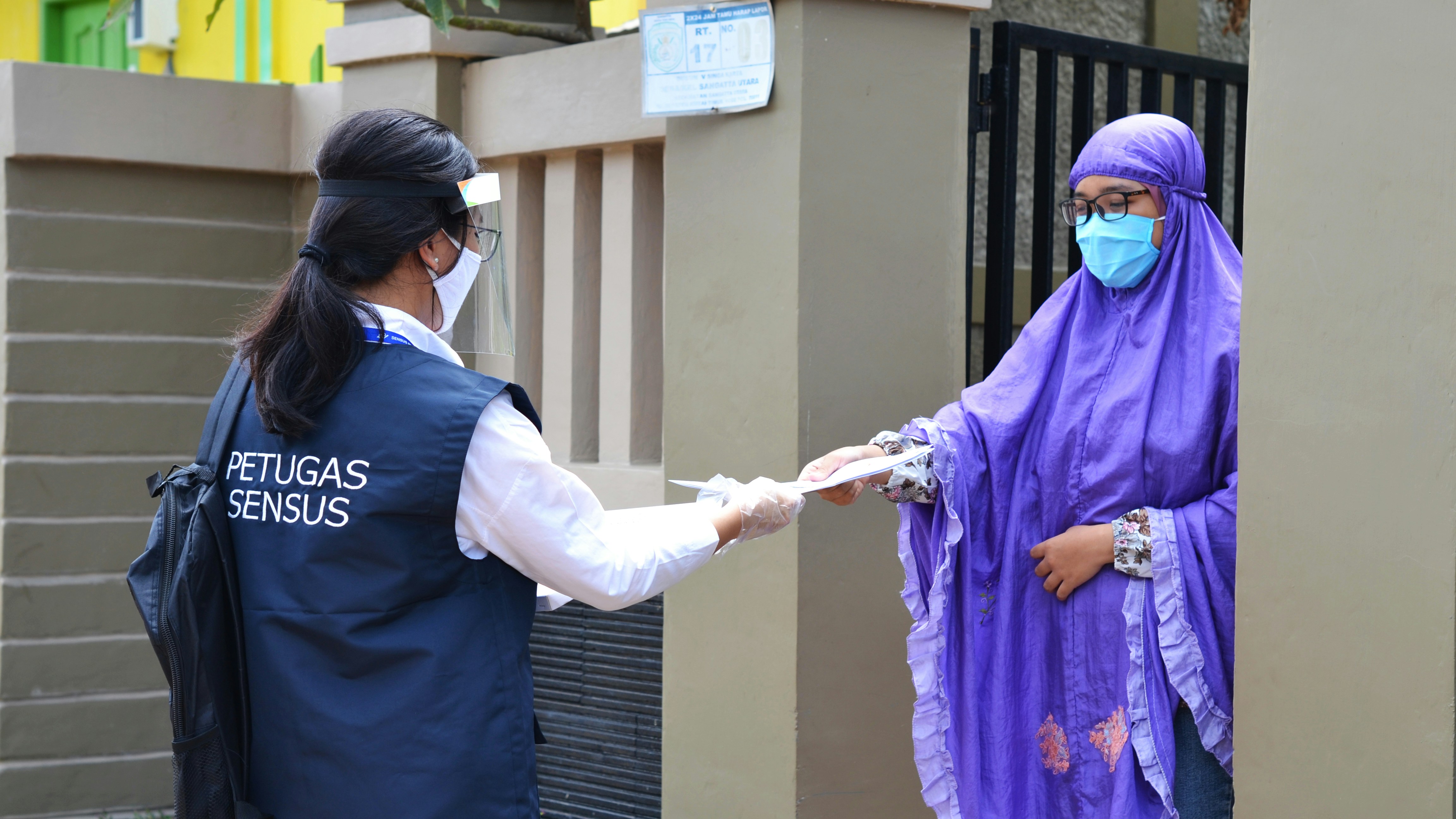 A census worker wearing protective gear, including a face mask, face shield, gloves, and a vest labeled 