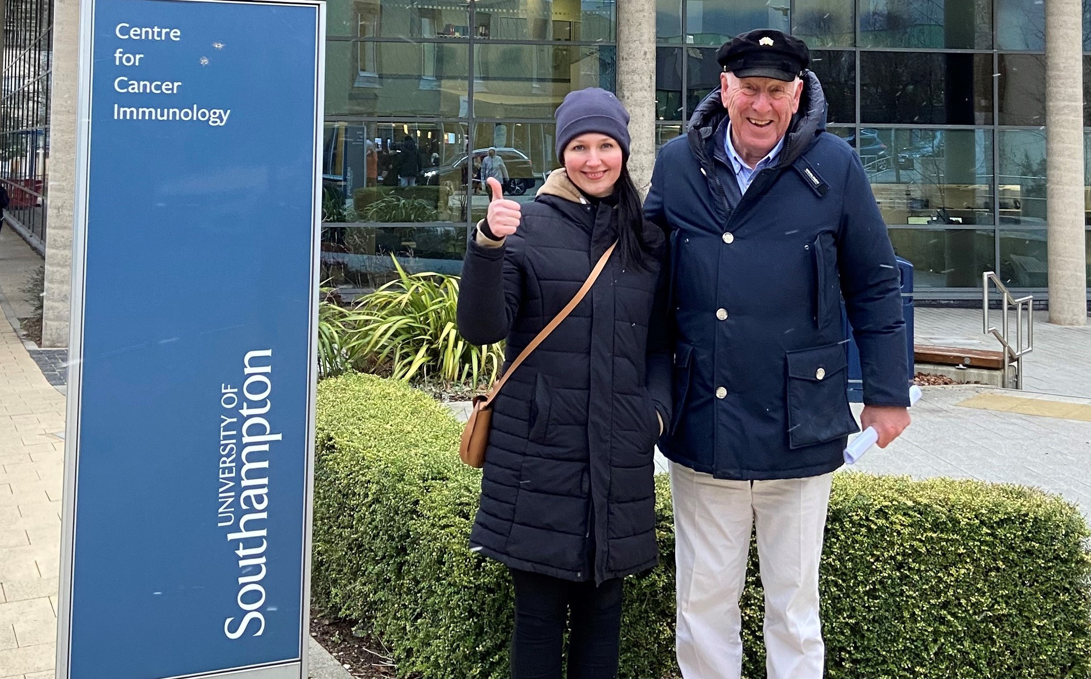 Woman and man in coats and hats standing next to a blue ’University of Southampton’ sign 
