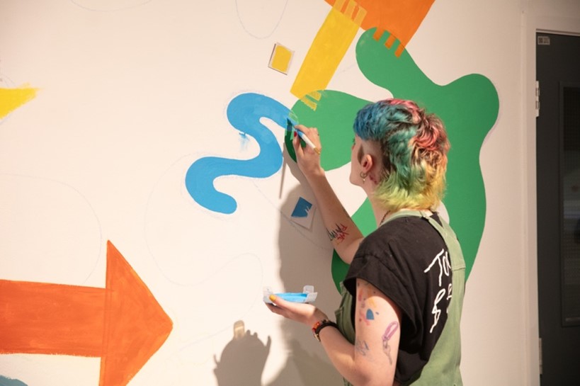 An artist paints a colourful mural on a wall