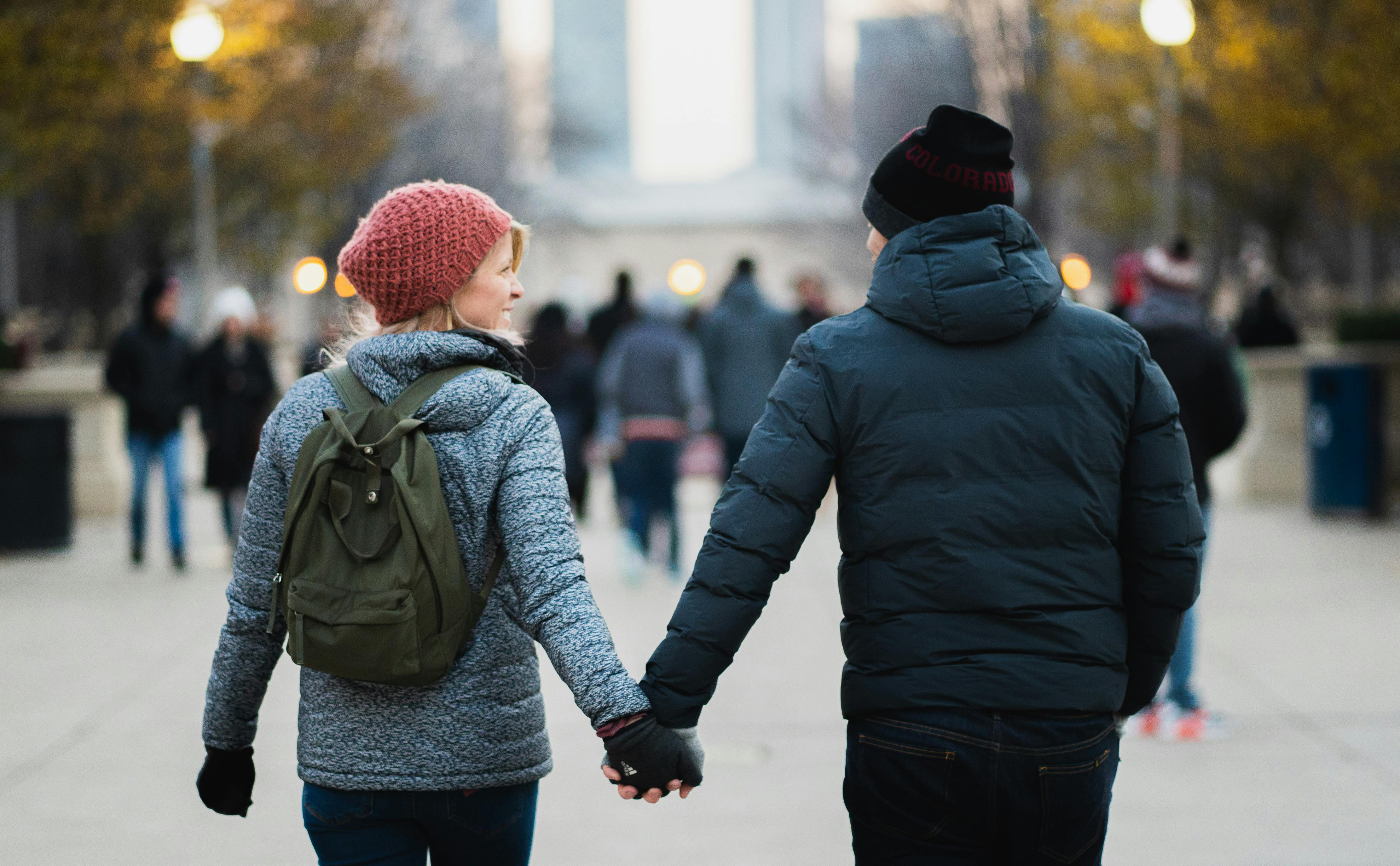 Man and a woman in a street, dressed in winter clothing, holding hands and walking away from the camera.