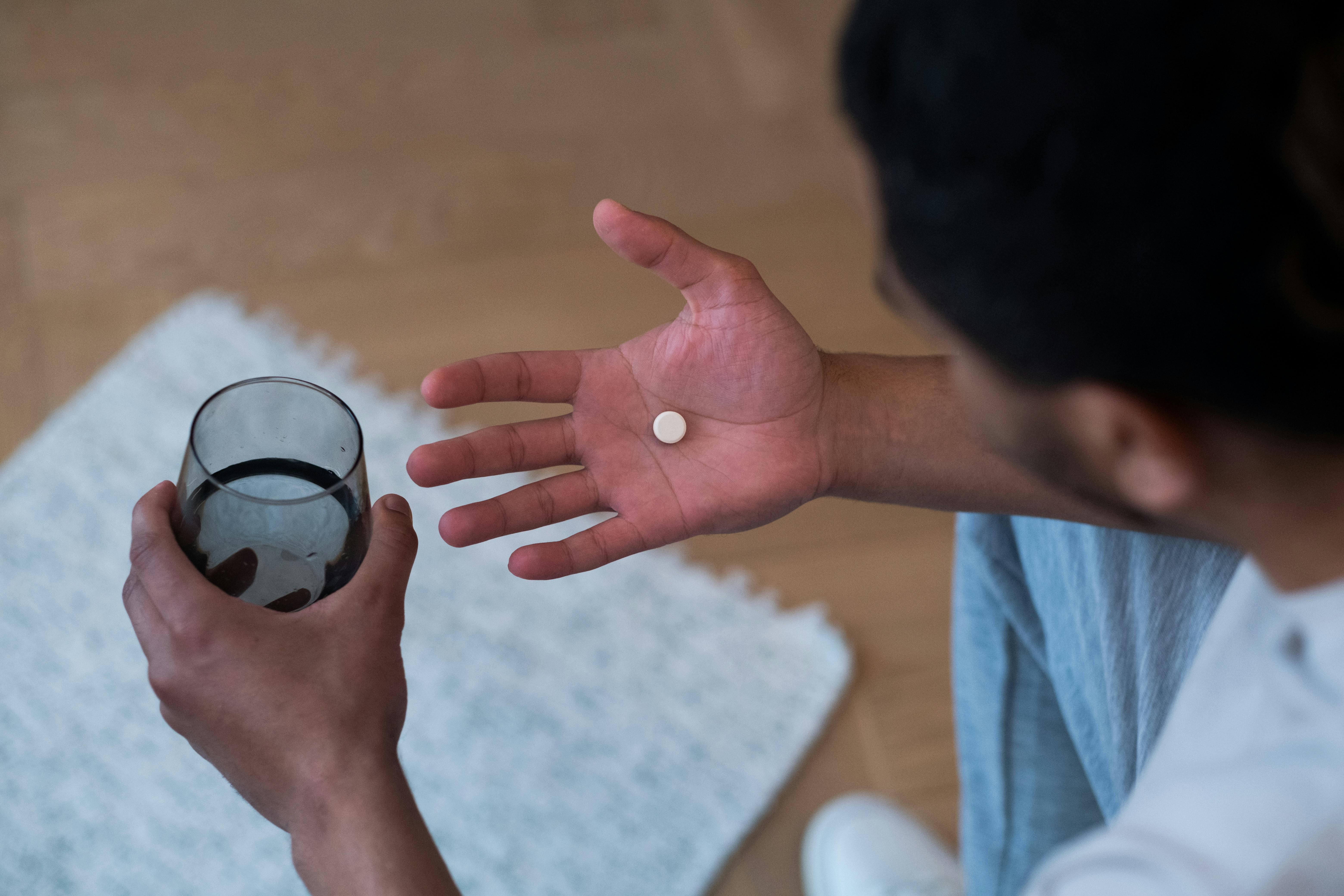 Man holding pill in one hand and glass of water in the other.
