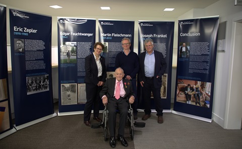 Three people standing and one man sat in a wheelchair, in front of a selection of pull-up banners. 