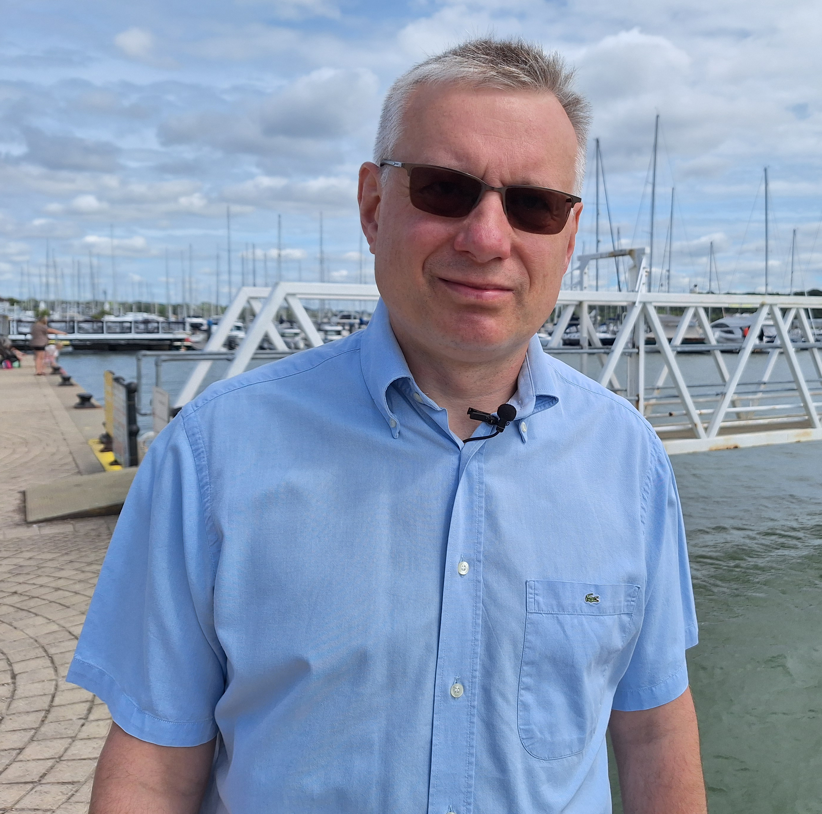 Waist high view of man standing on a river quay wearing a blue shirt and looking to camera.