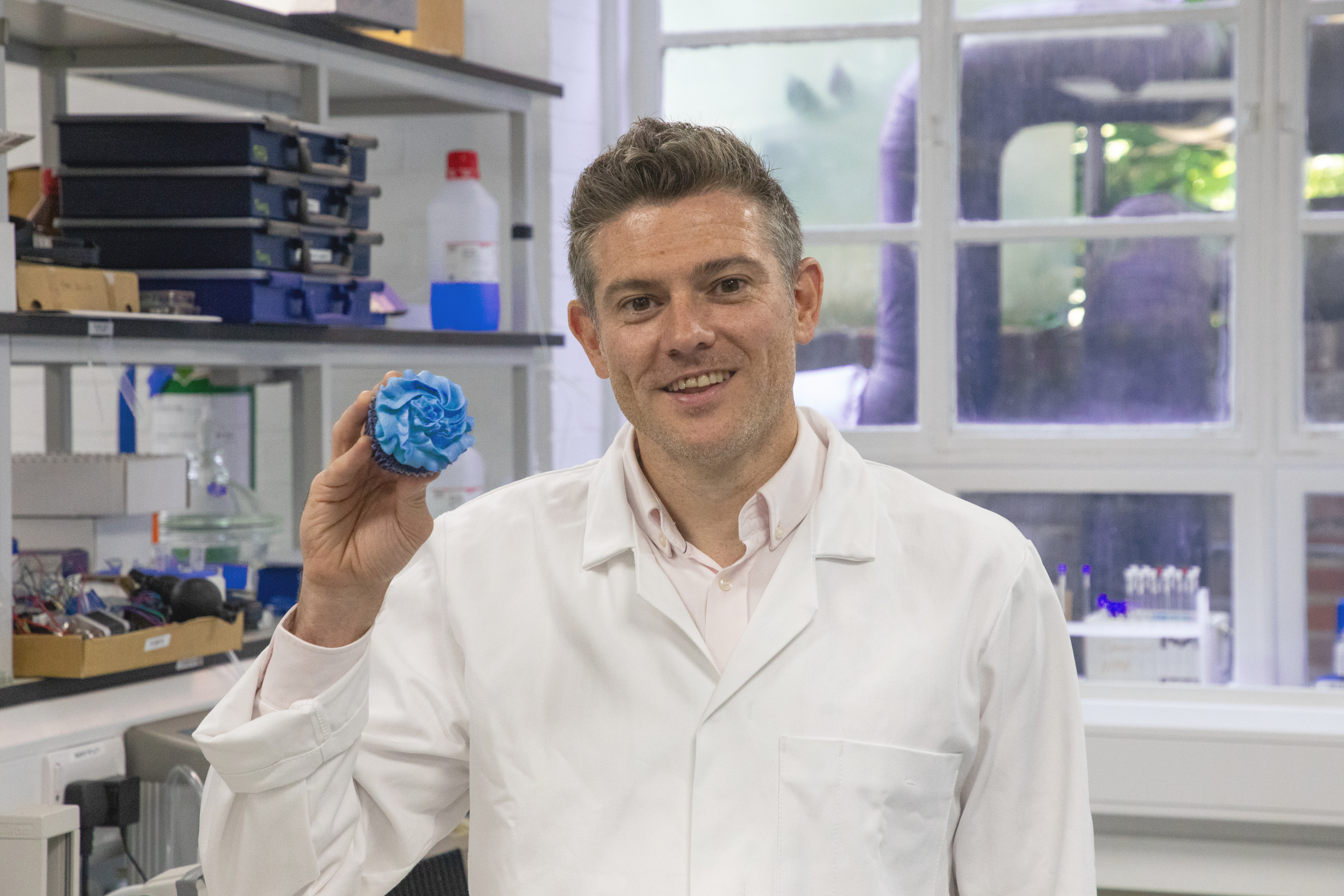 Professor Jon Swann in white lab coat holding a blue muffin
