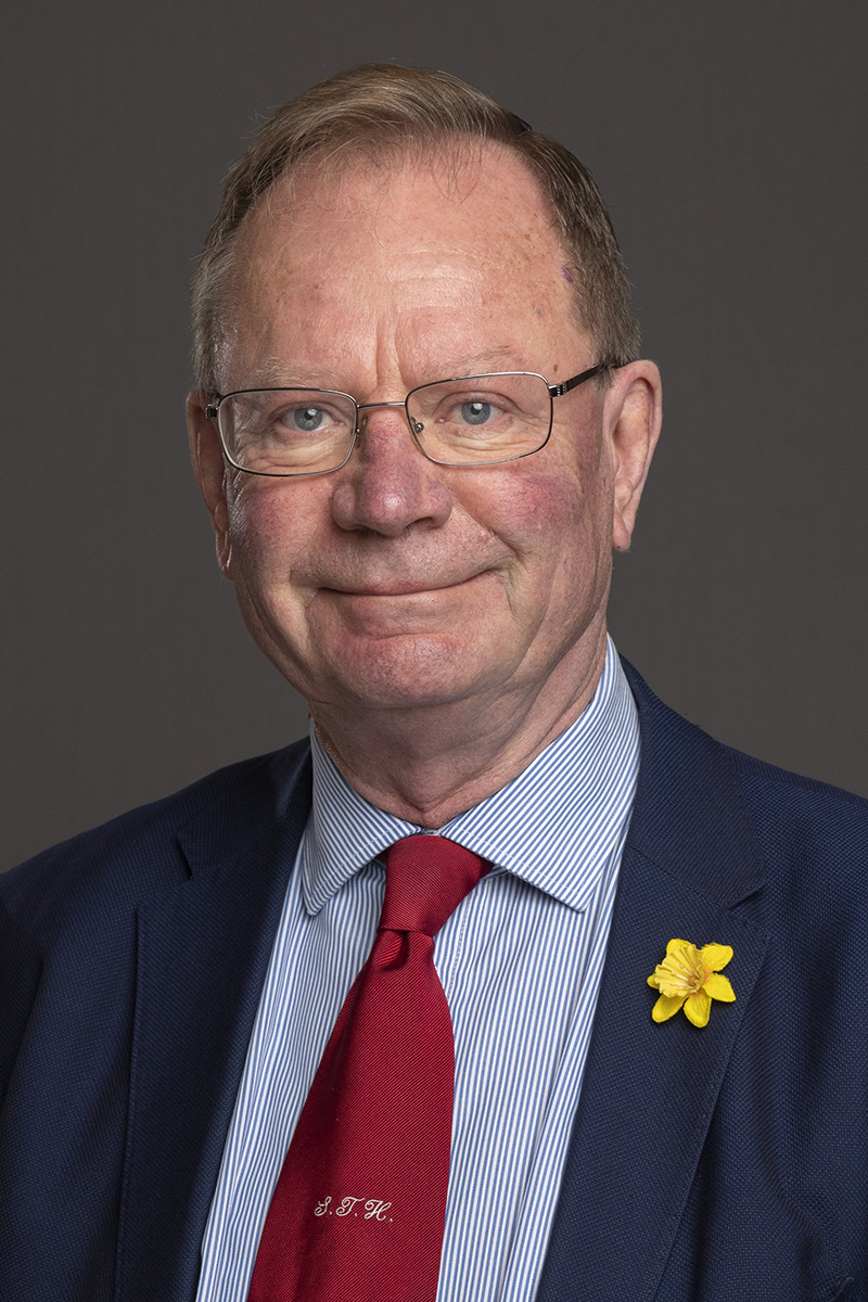 Head and shoulders view of man wearing glasses and a dark blue suit with a red tie.