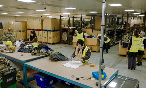 People wearing high vis jackets standing inside a large warehouse full of camouflage clothing.