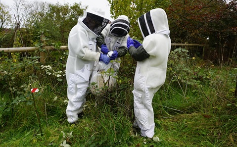 Three people in white boilersuits and protective head gear holding a large clear plastic bag