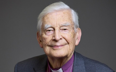 A white-haired older man softly smiles looking at the camera