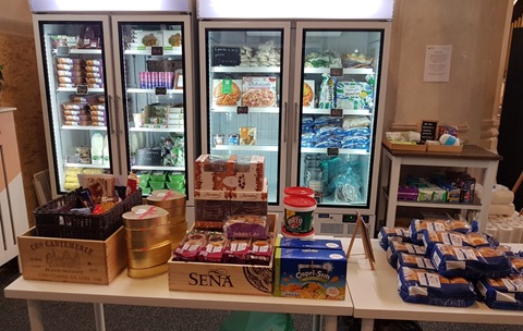 Fridges full of food with a table in front with packets of food and drink on it