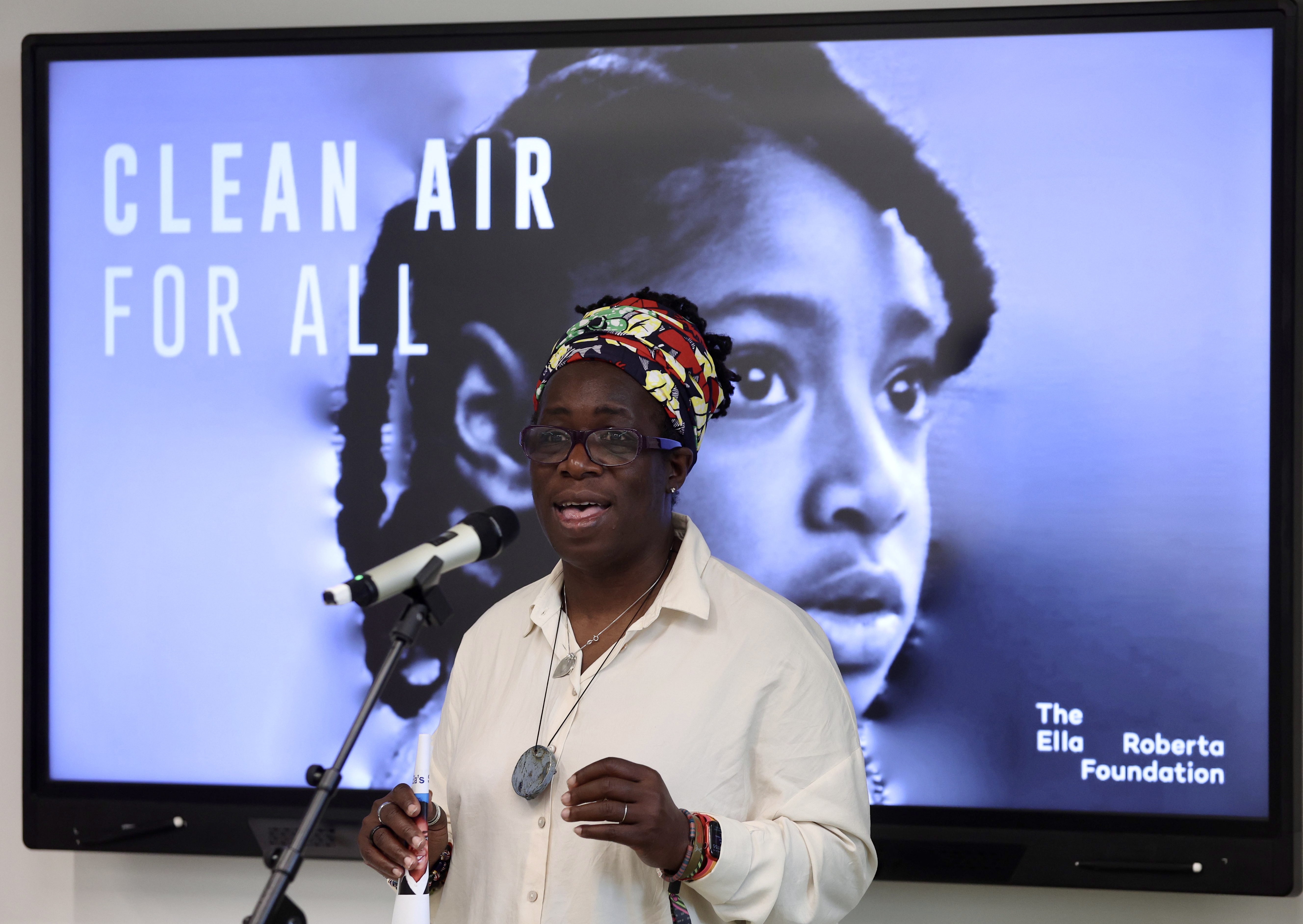 Clean air campaigner Rosamund Adoo-Kissi-Debrah CBE speaking in front of a presentation slide showing her daughter Ella and reading ’Clean air for all’