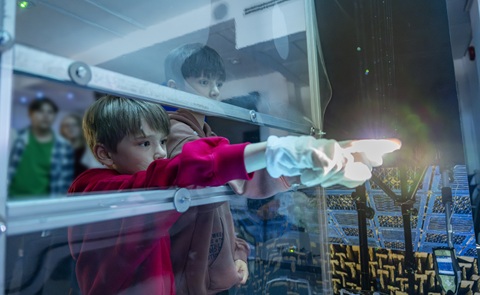 A young boy in a red jumper is reaching his hand into a container full of light