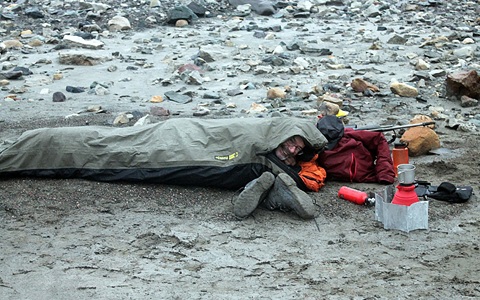 Man lying in sleeping bag outdoors on a rocky surface