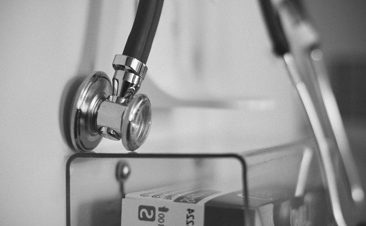 A black and white image of a stethoscope hanging in a blurred medical setting.