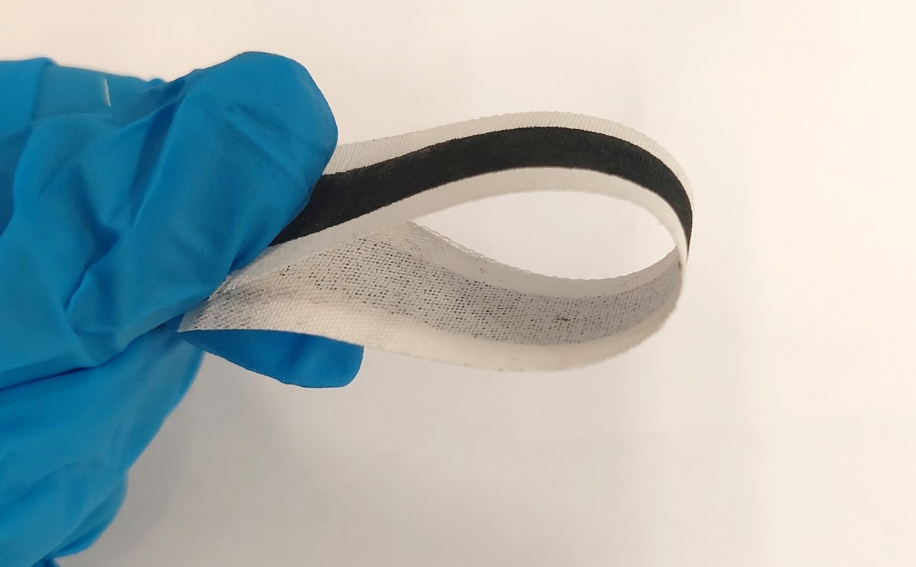 A blue rubber gloved hand with fingers holding a strip of black and white e-textiles material in a loop shape.