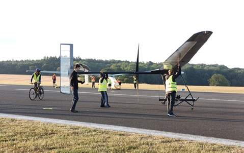 A group of people wearing high vis standing around the sides of a large glider-style plane, on a runway