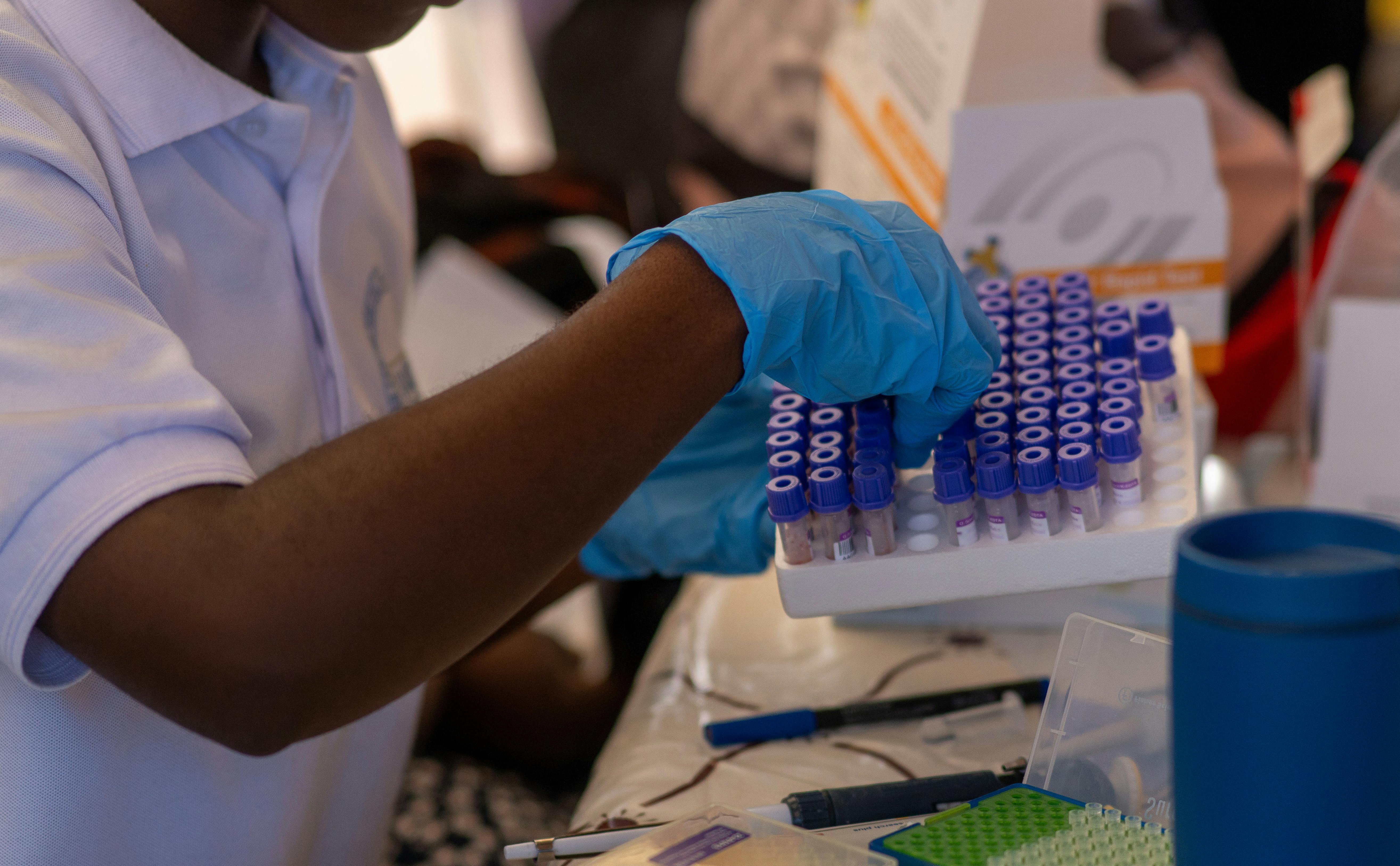 A person is taking medical sample tubes out of a tray holding them upright in a lab