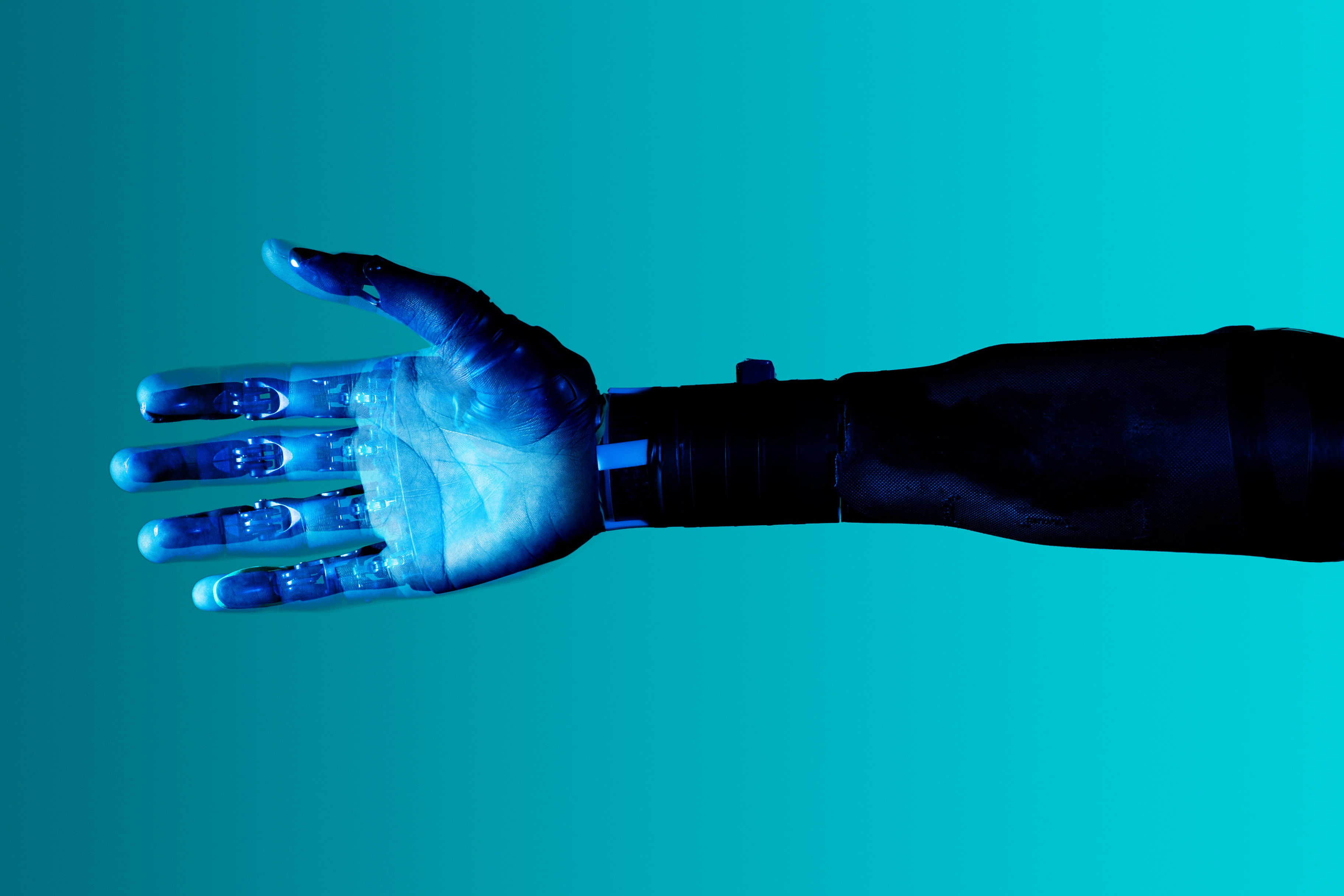 A high tech prosthetic arm and hand against a blue background. The prosthetic hand is open with fingers extended, revealing a detailed and intricate design, including individual mechanical joints and components. 