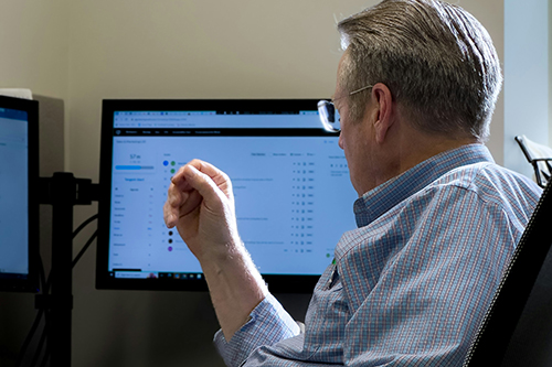 Researcher sitting at a computer and examining data displayed on two monitors.