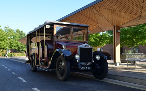 A vintage bus parked next to a large modern wooden bus shelter, under a blue sky