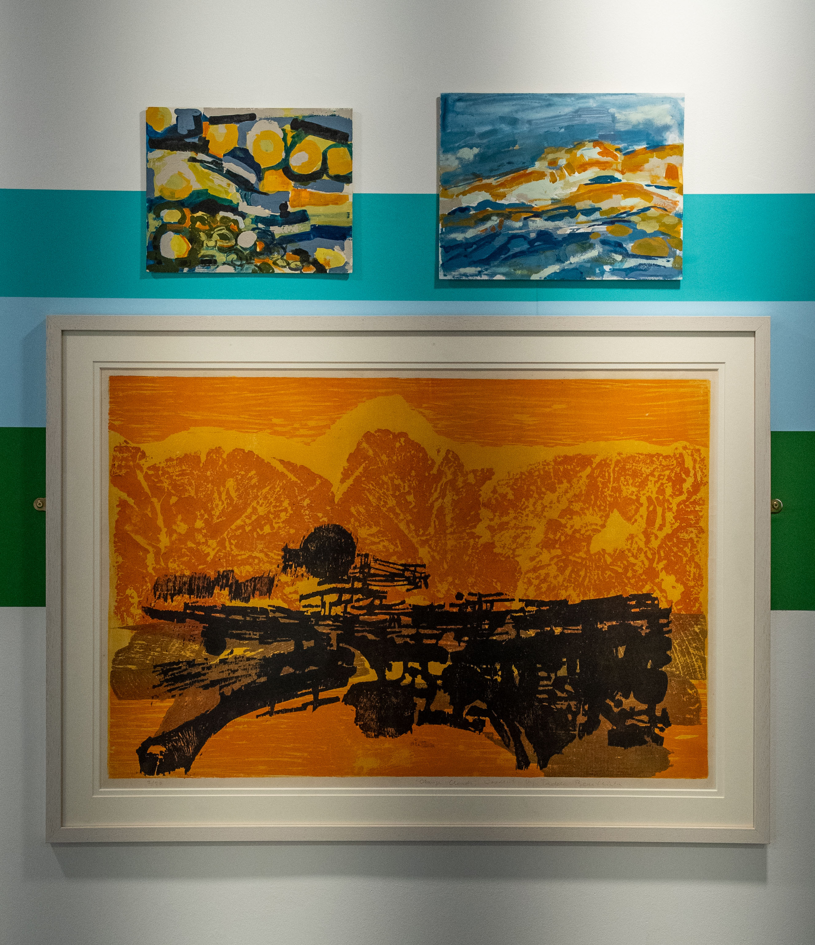 Three abstract style paintings mounted on a wall. One large with two smaller ones above.