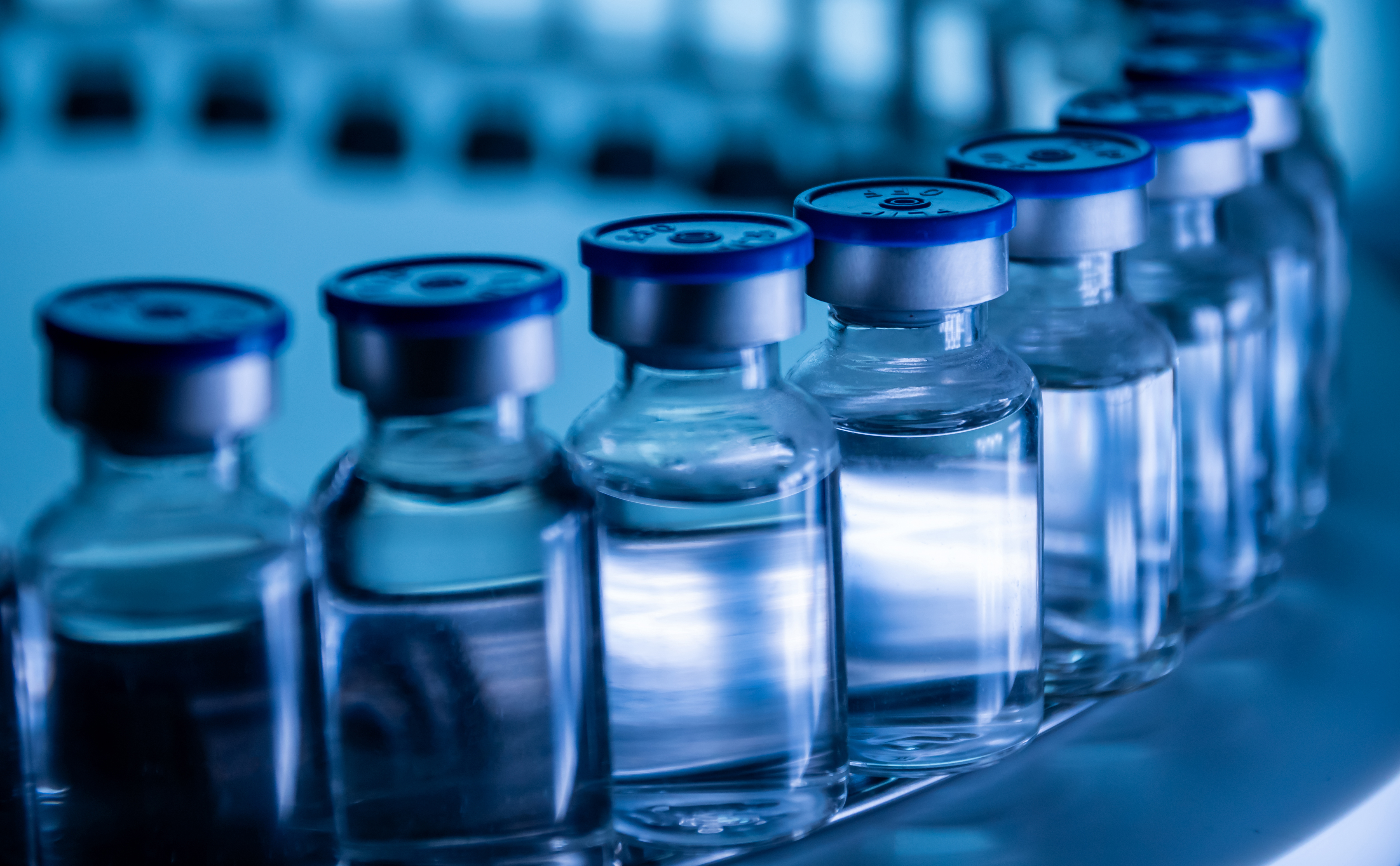 Curved row of transparent vaccine bottles under a blue light