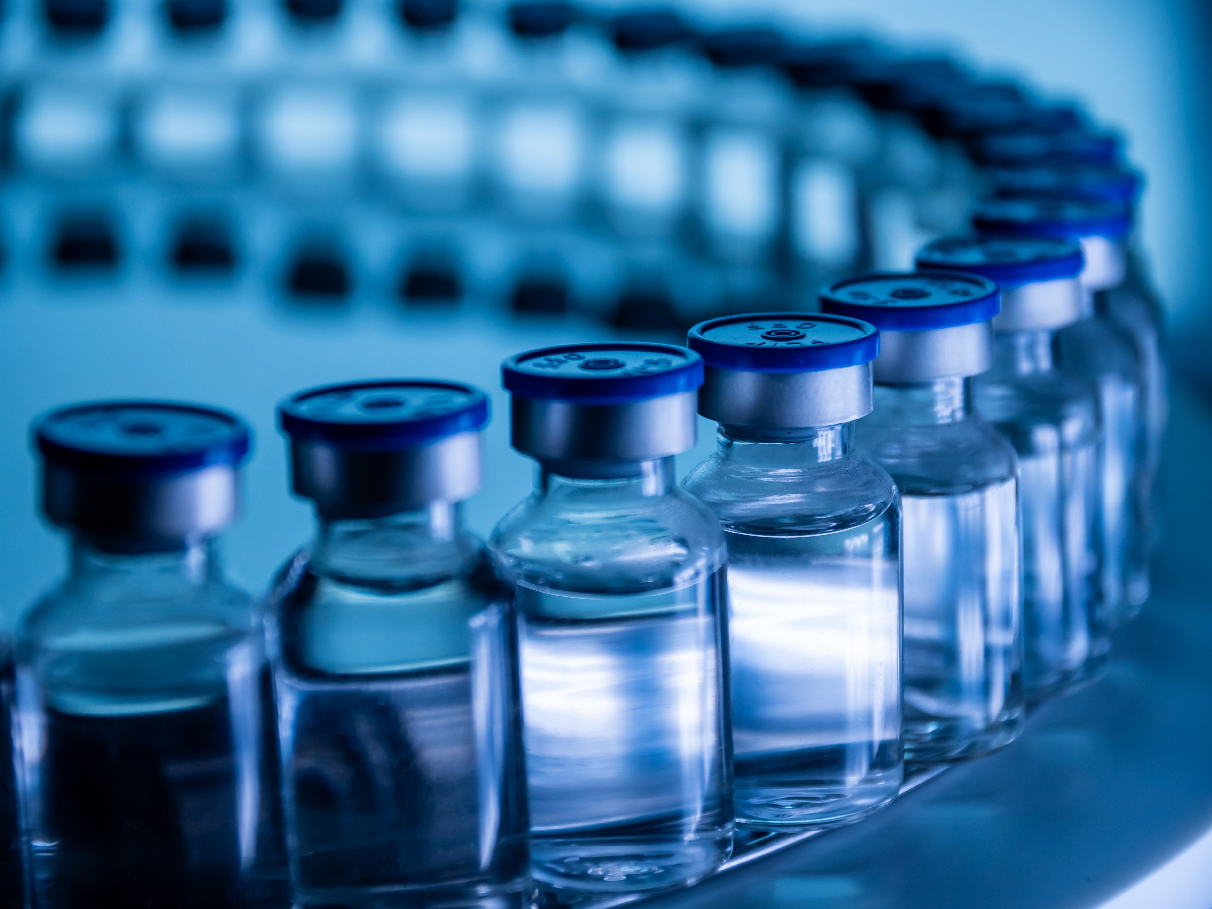 Curved row of transparent vaccine bottles under a blue light