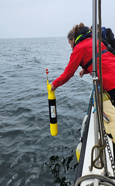 Scientist leaning over the side of a boat lowering a mini submarine vertically into the sea.