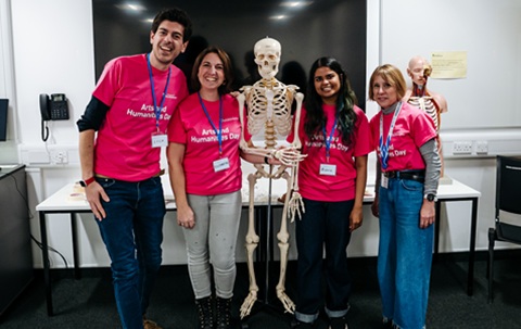 Four people in pink T-shirts standing in front of a large TV screen, with a skeleton in the centre of the group