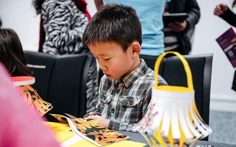 Young boy sitting at a table cutting out a shape in a piece of paper