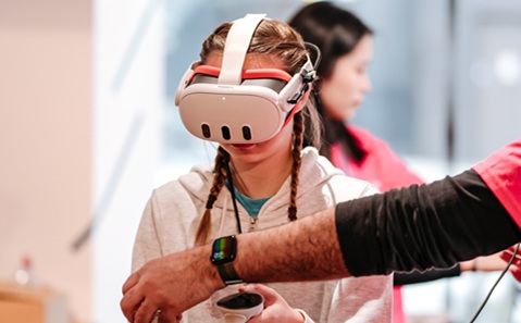 A young girl wearing a VR headset and holding VR controllers in both hands