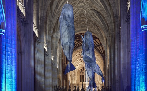 Two large scupltures of sperms whales hanging from the roof inside a large church