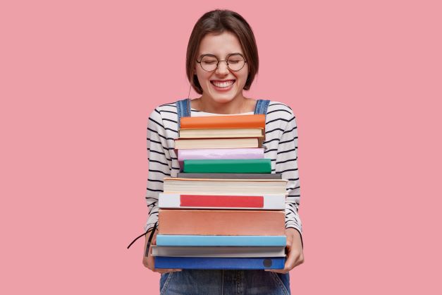 A woman looking excited with her eyes closed holding a large pile of books